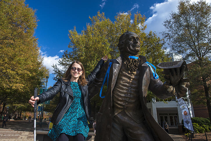 Person with a cane for the vision impaired standing with the statue of George Mason.