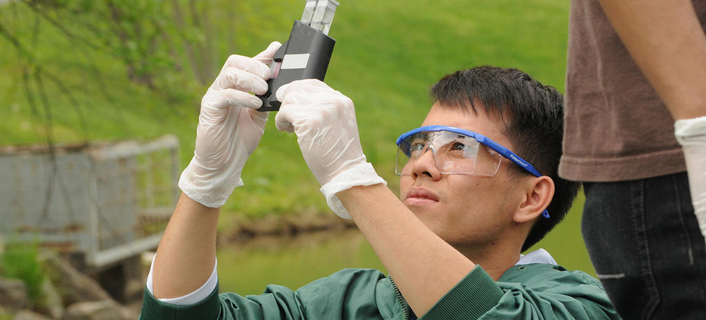 Student with safety goggles outdoors testing water levels/contaminants.