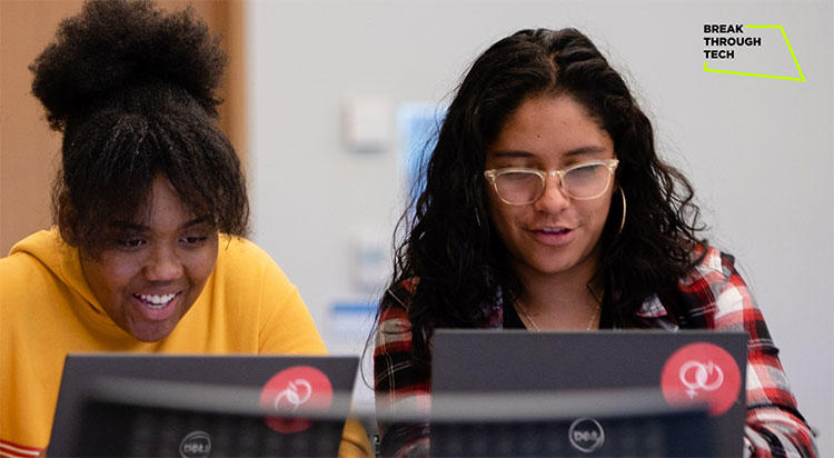 Two girls sitting in front of computers in a computer lab-like room.