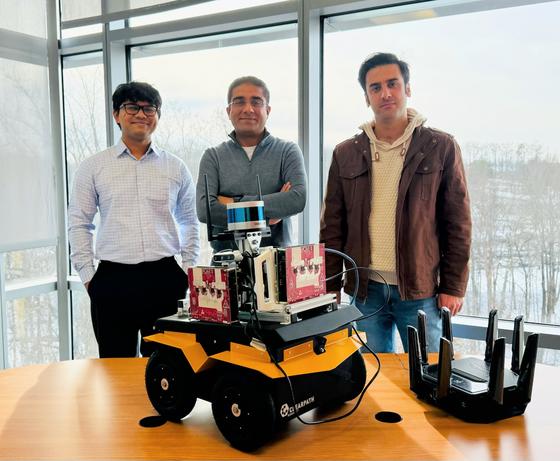 Three men stand in front of a robot vehicle